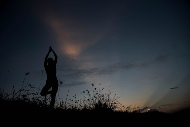 Silhouette of a young woman practicing yoga at sunset