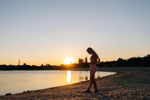 Silhouette of young woman stepping on Sadhu board with nails during concentration meditation practice on sandy beach of sunlight at summer sunset