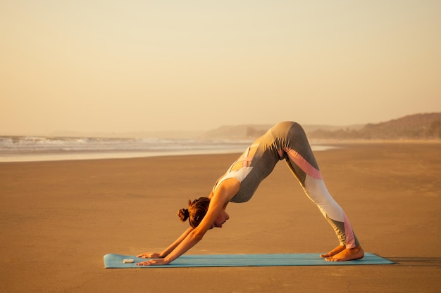 Silhouette of young woman in a stylish suit for yogi jumpsuit doing yoga on the beach in pose copy space