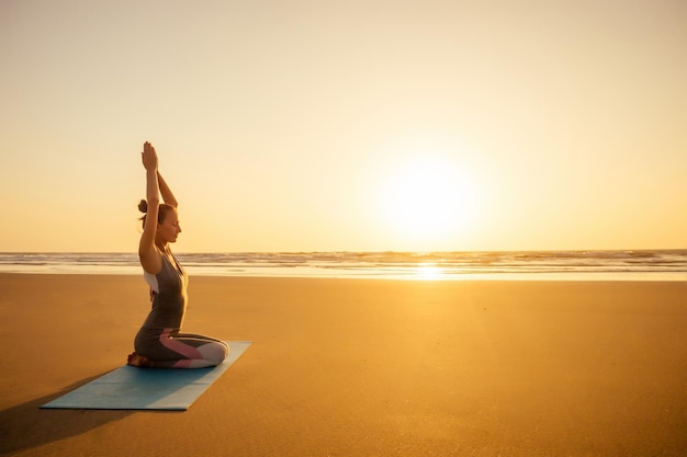 Silhouette of young woman in a stylish suit for yogi jumpsuit doing yoga on the beach in pose copy space