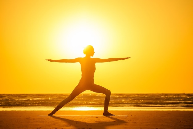 Silhouette of young woman in a stylish suit for yogi jumpsuit doing yoga on the beach in pose copy space.