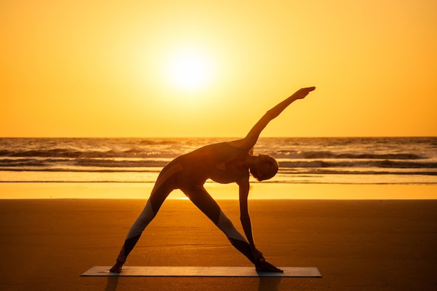 Silhouette of young woman in a stylish suit for yogi jumpsuit doing yoga on the beach in pose copy space