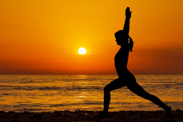 Silhouette of young woman in a yogi suit  doing yoga on the beach  in sunset time.