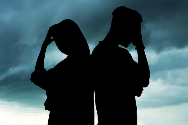 Silhouettes of arguing couple against sky with heavy rainy clouds Relationship problems