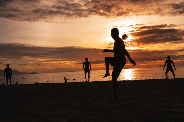 Silhouettes of Asian men ball players playing traditional beach soccer sepak takraw by sea in summer at sunrise