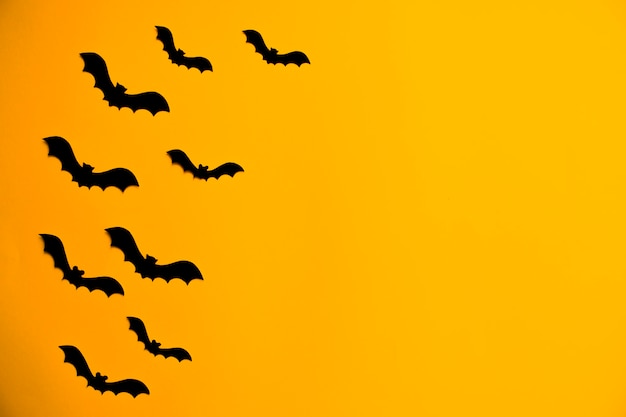 Silhouettes of black bats made of paper on orange background. Halloween greeting card