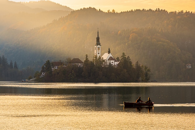 Silhouettes of a couple floating on a boat near the Bled island at beautiful sunset light