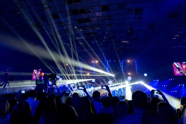 Silhouettes of crowds of spectators at a concert with smartphones in their hands. The scene is beautifully illuminated by spotlights.