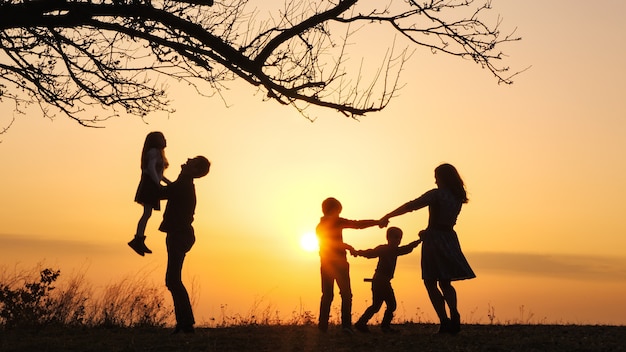 Silhouettes of family spending time together in the meadow near during sunset