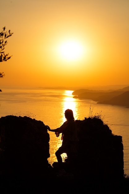 Silhouettes of a girl against the background of the sea and the setting sun