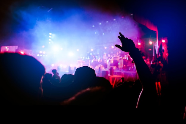 Silhouettes of hand in concert.Light from the stage.confetti.the crowd of people silhouettes with their hands up.ribbon