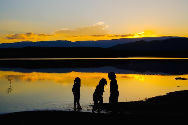 Silhouettes of happy children playing on the lake at the sunset time, Reservoir Amphoe Wang Saphung Loei Thailand