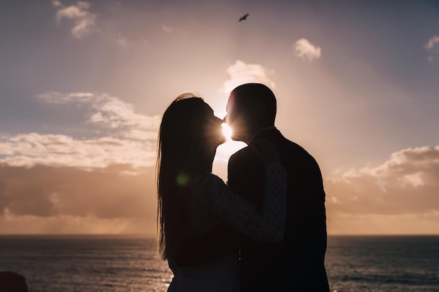 Silhouettes of kissing newlyweds on sunset and ocean background