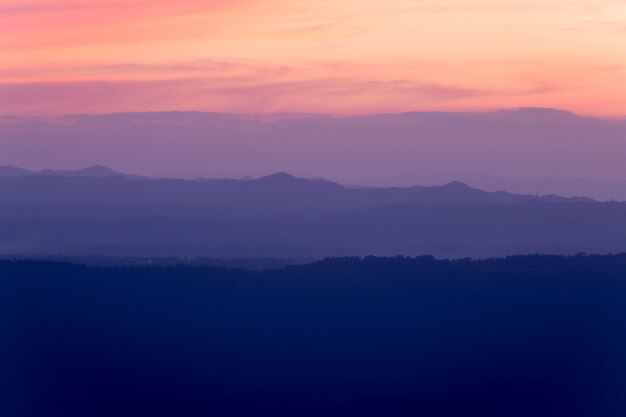 Silhouettes of the mountain hills layer in the morning mist. Colorful summer scene.