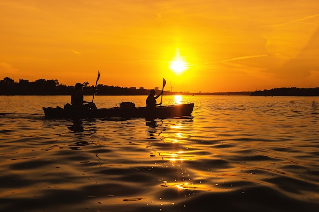 Silhouettes of people in boat at sunset Man and woman ride boat on river Small family trip