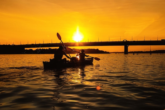 Silhouettes of people in kayak at sunset Young married couple is boating on river