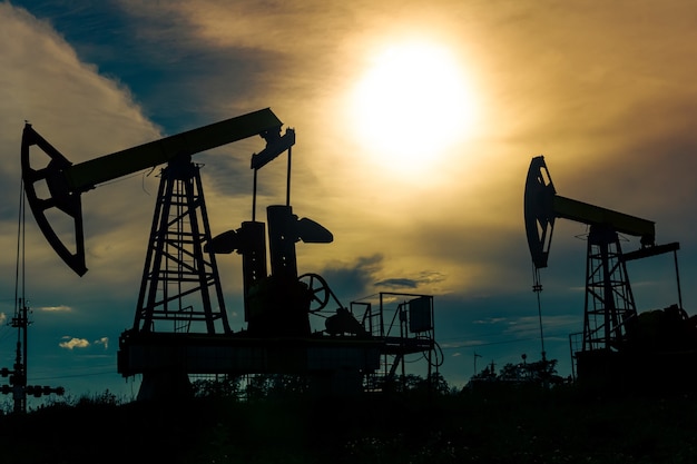 Silhouettes of pumpjacks with piston pump on an oil wells against the background of an alarming sky