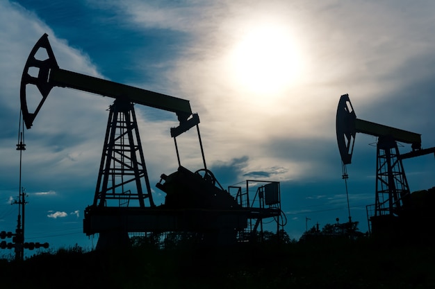 Photo silhouettes of pumpjacks with piston pump on an oil wells against the background of an alarming sky