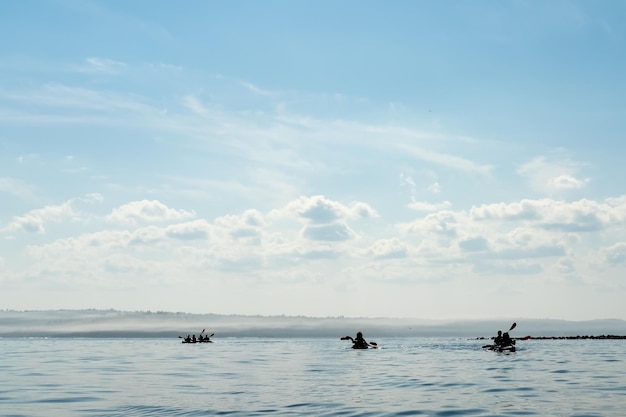 Silhouettes of three kayaks with tourists floating on the lake against the horizon