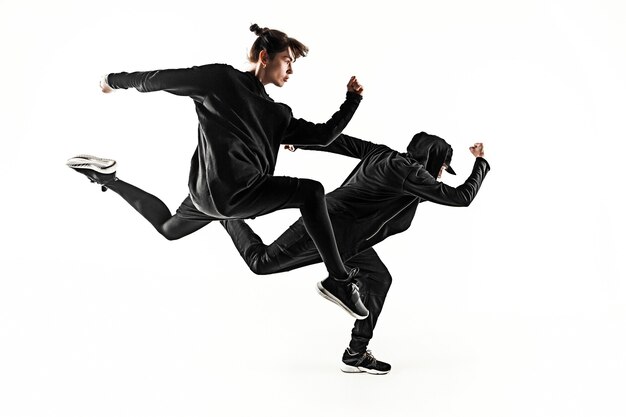 The silhouettes of two young hip hop male and female break dancers dancing on white studio background