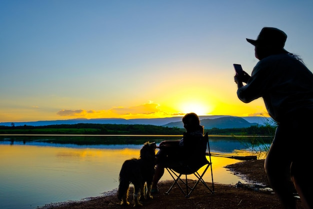 Silhouettes of two young women taking a photo over gray background on the lake at the sunset time