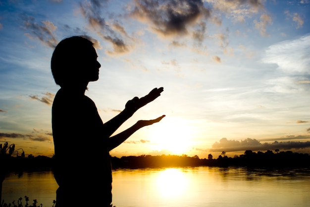 silhouettes Women praying hand over beautiful sun set background