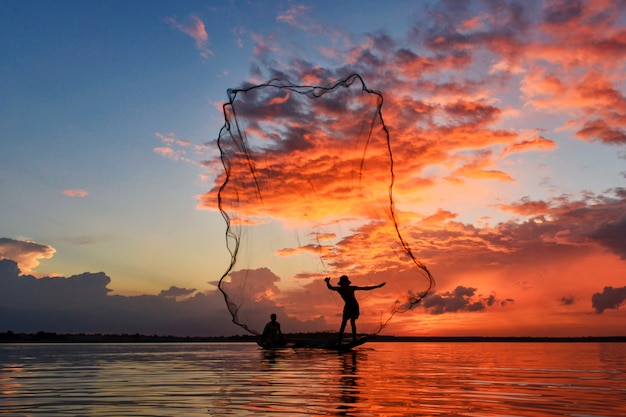 Silluate fisherman and boat in river on during sunrset, fisherman trowing the nets on during sunset, during sunset, Thailand