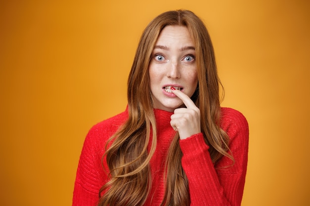 Silly, cute redhead woman making innocent oops expression holding finger on lip and looking scared with questioned expression at camera making mistake and trying get away of troubles with flirty gaze