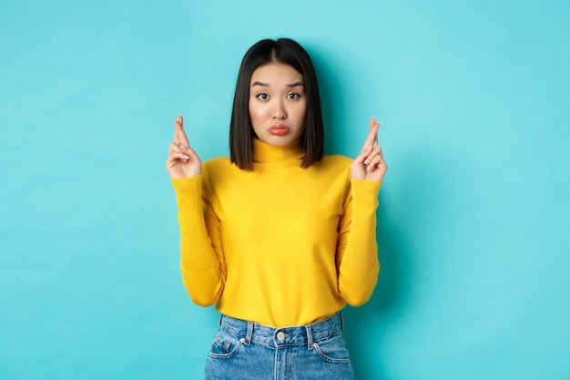 Silly hopeful asian girl making wish, pucker lips and looking at camera with dreamy glance