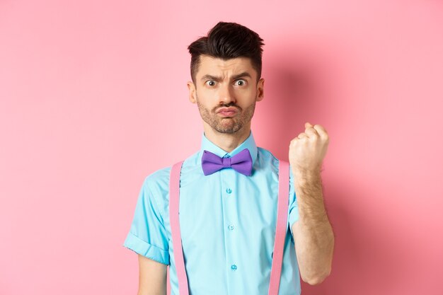 Silly man scolding someone, threaten person with fist, looking grumpy and disappointed, standing on pink background.