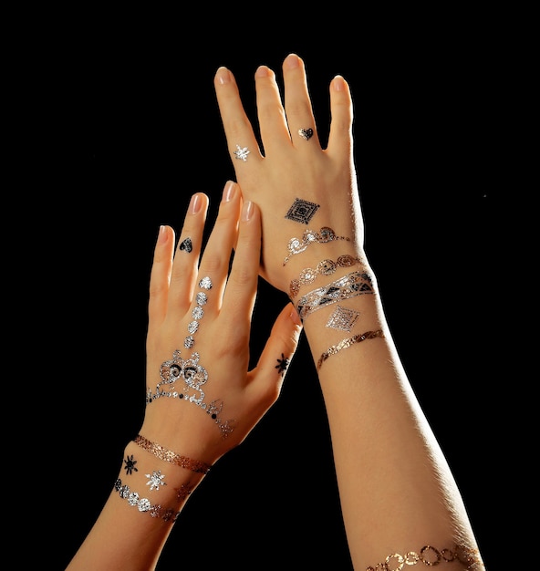 Silver and golden flash tattoo on female hands over black background