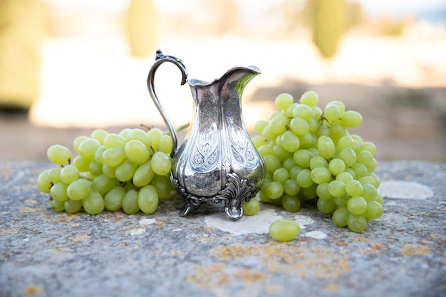 Silver jug with wine and bunches of white grapes Still life