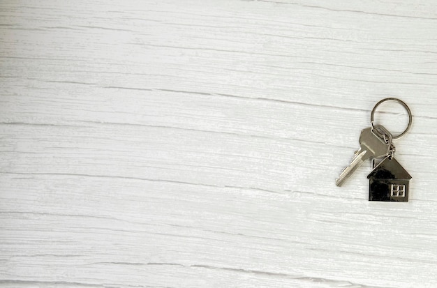 Silver key with silver house figure on white wooden background buying new house real estate concept ...