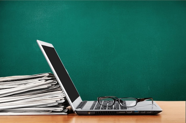 Silver laptop with glasses and heap of papers