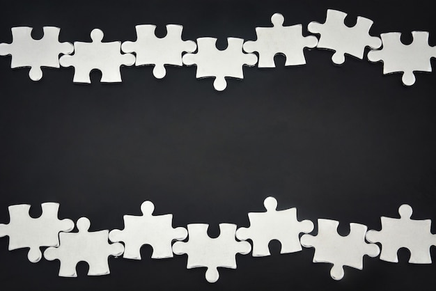 Silver metal puzzle pieces arranged as a frame on black background business partnership concept