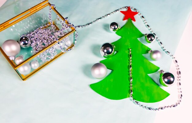 Silver ornaments come out of a glass and gold casket and decorate a flat Christmas tree on a black and blue background