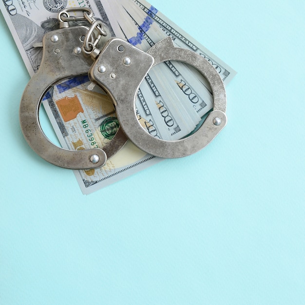 Photo silver police handcuffs and hundred dollar bills lies on light blue background