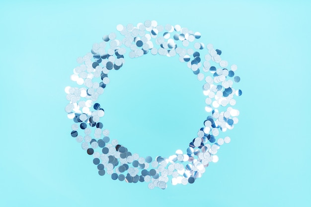 Silver shiny confetti in the form of a round frame on a blue background with a copy of the space.