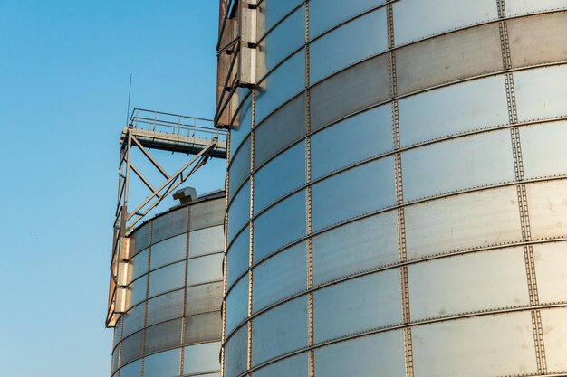 Silver silos on agro manufacturing plant for processing drying cleaning and storage of agricultural products flour cereals and grain Large iron barrels of grain Granary elevator