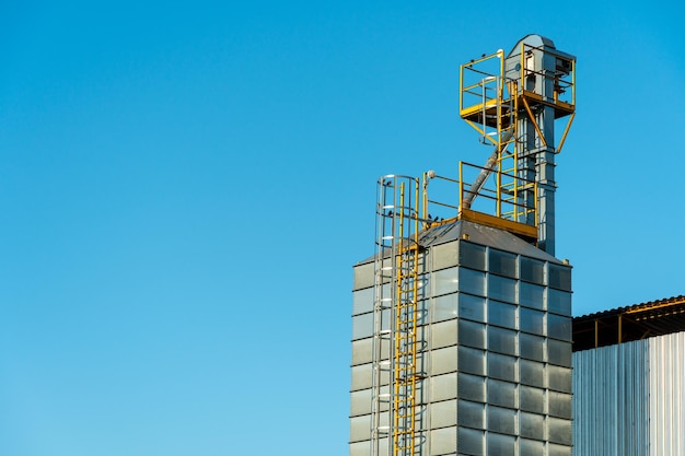 Photo silver silos on agro manufacturing plant for processing drying cleaning and storage of agricultural products flour cereals and grain large iron barrels of grain granary elevator