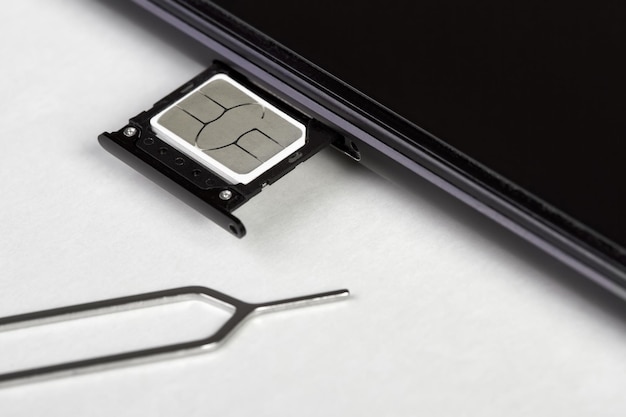 SIM card on the sim card tray of a smartphone on light background with pin needle tray remover