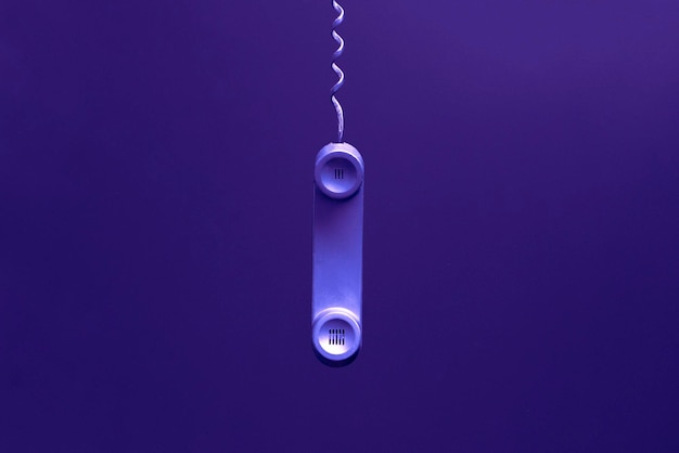 A simple dark old telephone handset with cable on pastel background