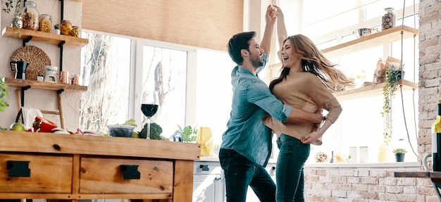 Simple joy of loving. Full length of beautiful young couple in casual clothing dancing and smiling while standing in the kitchen at home