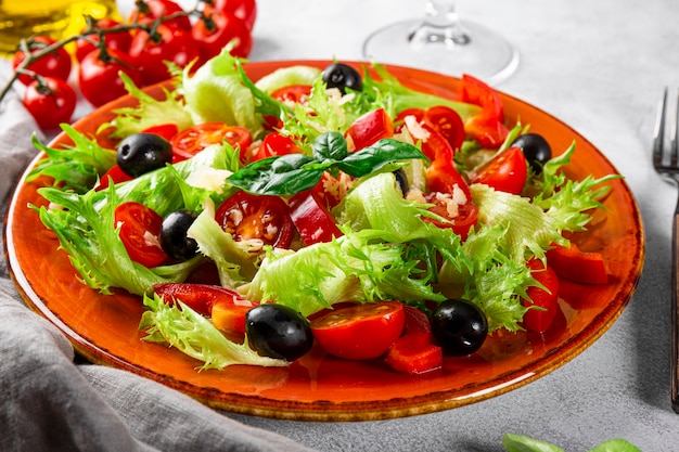 simple summer salad of lettuce tomatoes with olives and olive oil on a red plate closeup