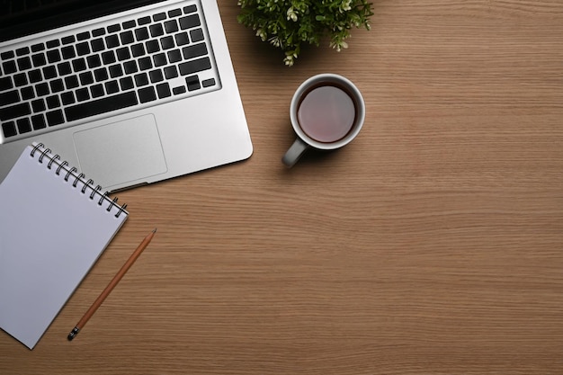 Simple workspace with laptop computer, coffee cup and notepad on wooden table.