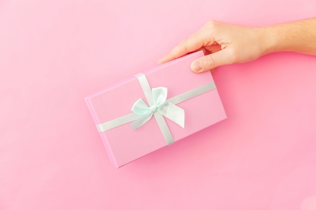 Simply design female woman hand holding pink gift box isolated on pink pastel colorful trendy background