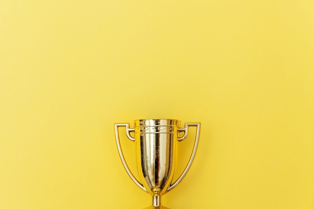 Photo simply flat lay design winner or champion gold trophy cup isolated on yellow colorful background