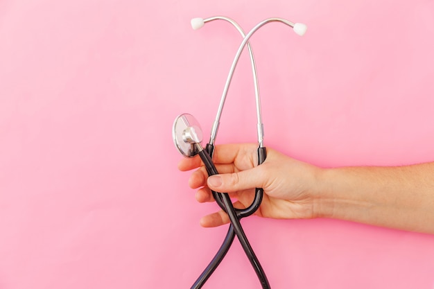 Simply minimal design woman hand holding medicine equipment stethoscope or phonendoscope isolated on trendy pastel pink surface. Instrument device for doctor. Health care life insurance concept.