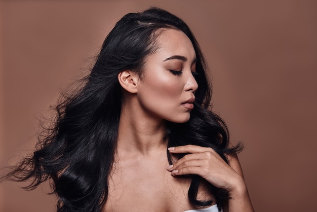 Simply stunning. Beautiful young woman keeping eyes closed while standing against brown background