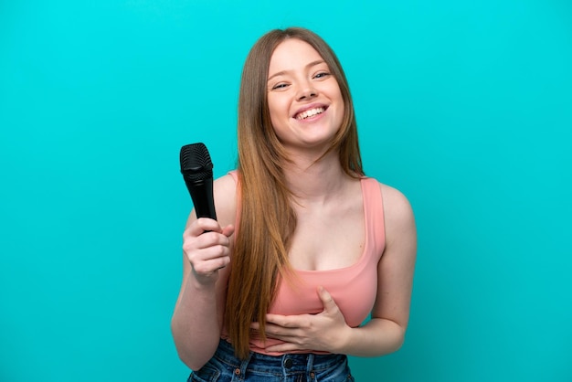 Singer caucasian woman picking up a microphone isolated on blue background smiling a lot